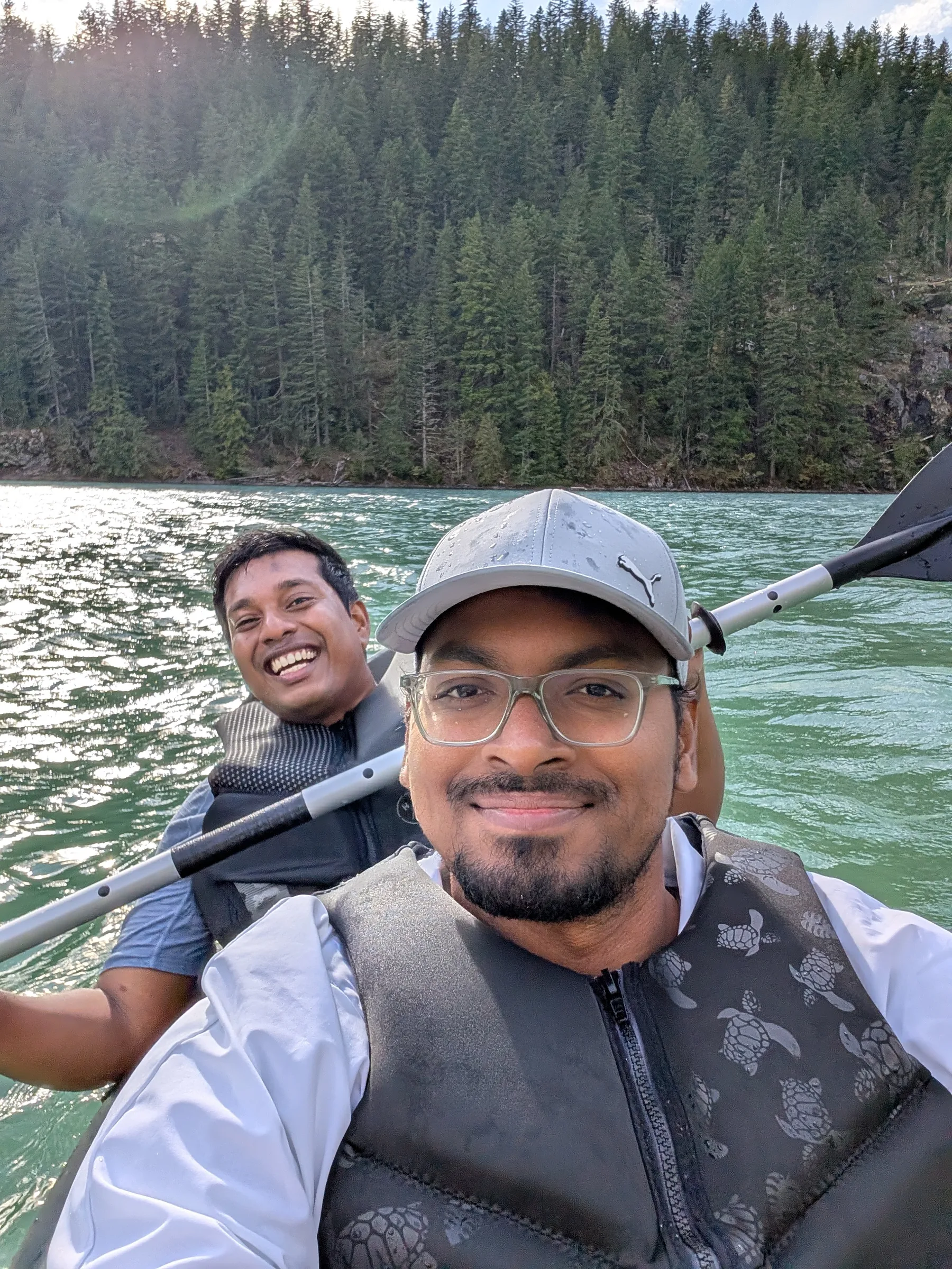 Selfie of two friends in life jackets kayaking on the turquoise water of Diablo Lake, with pine forest behind
