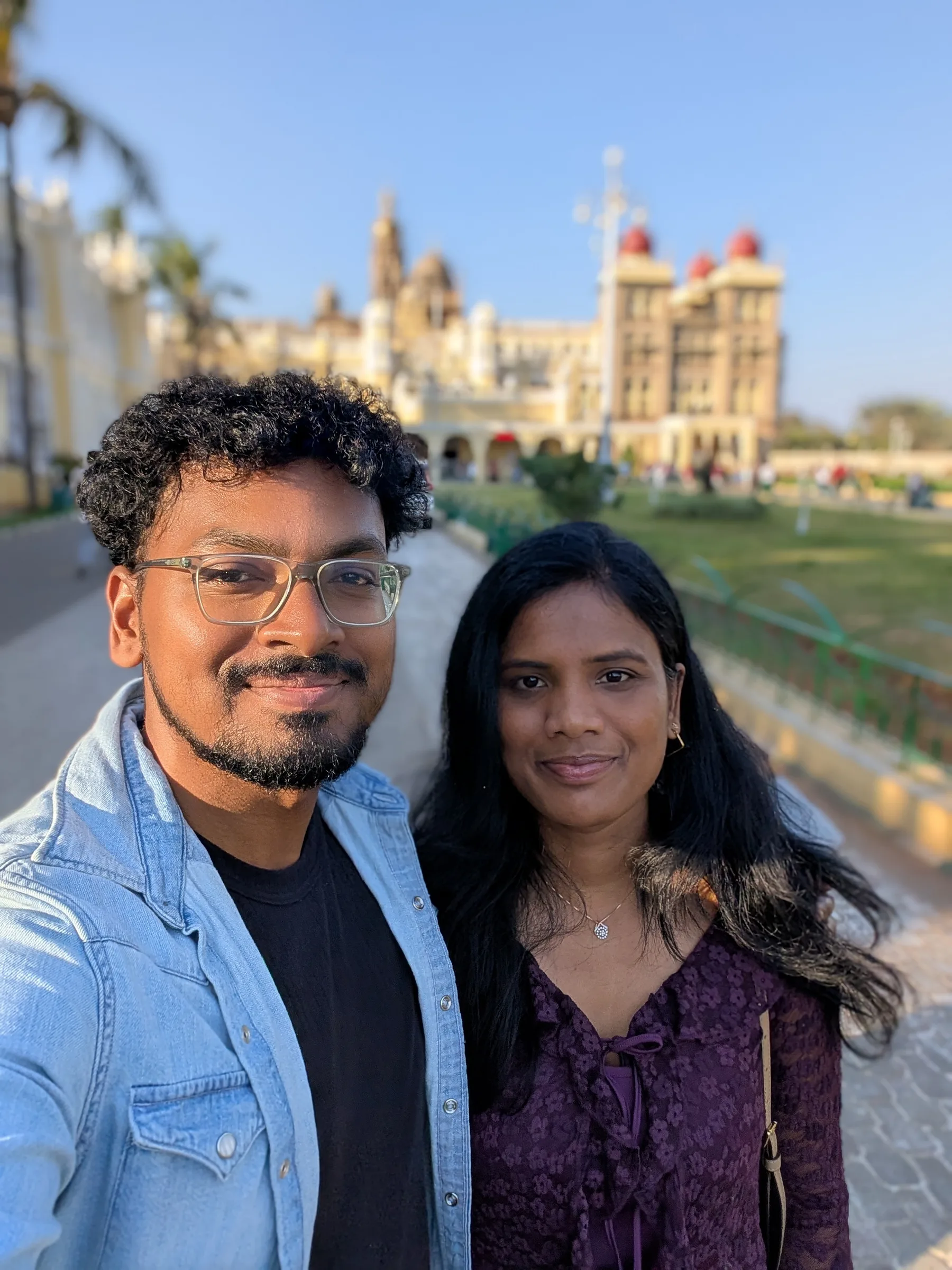 Selfie of two travellers in the grounds of Mysore Palace, its red domes behind them