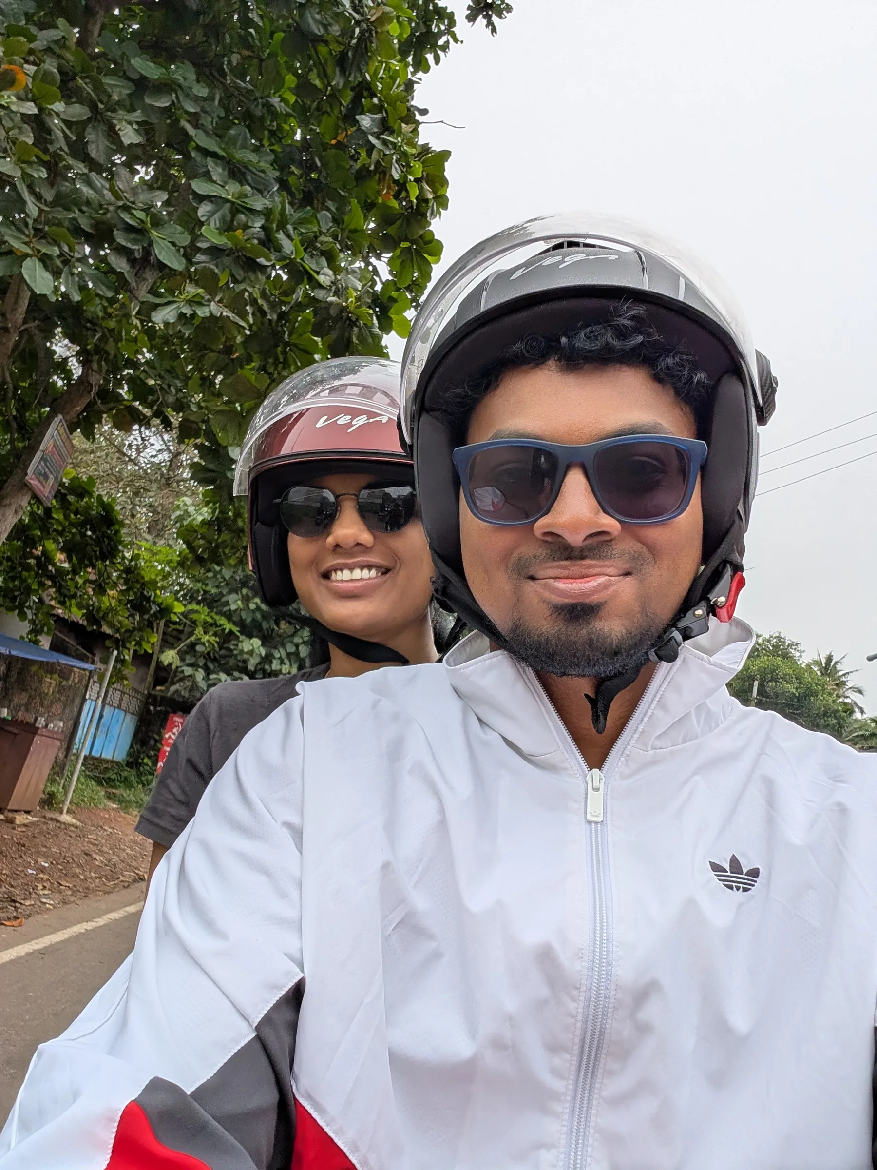 Selfie of two travellers in helmets riding a scooter down a tree-lined road in Varkala